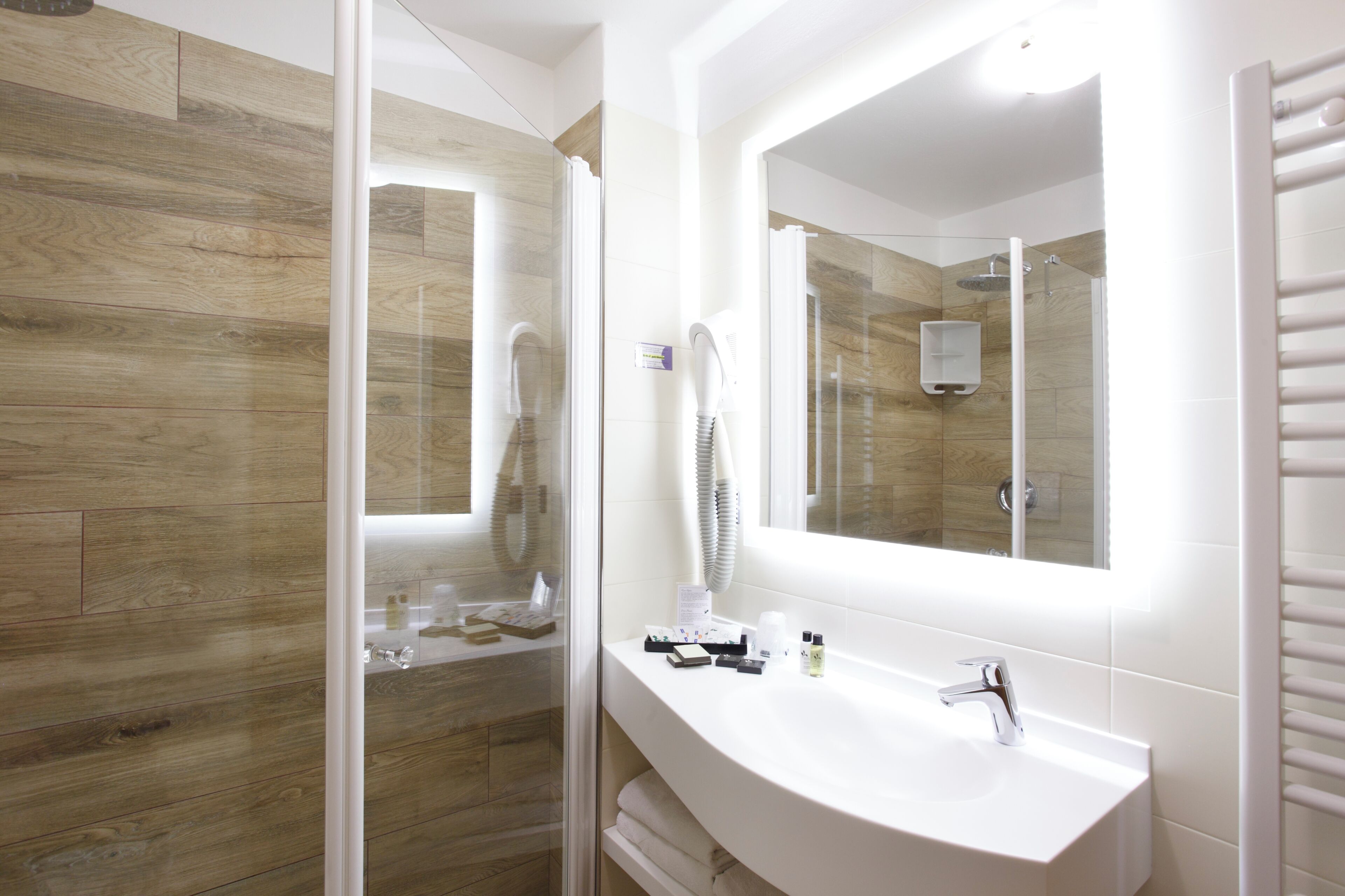 A modern bathroom with a wooden wall, a glass shower enclosure, a white sink, and a large mirror.
