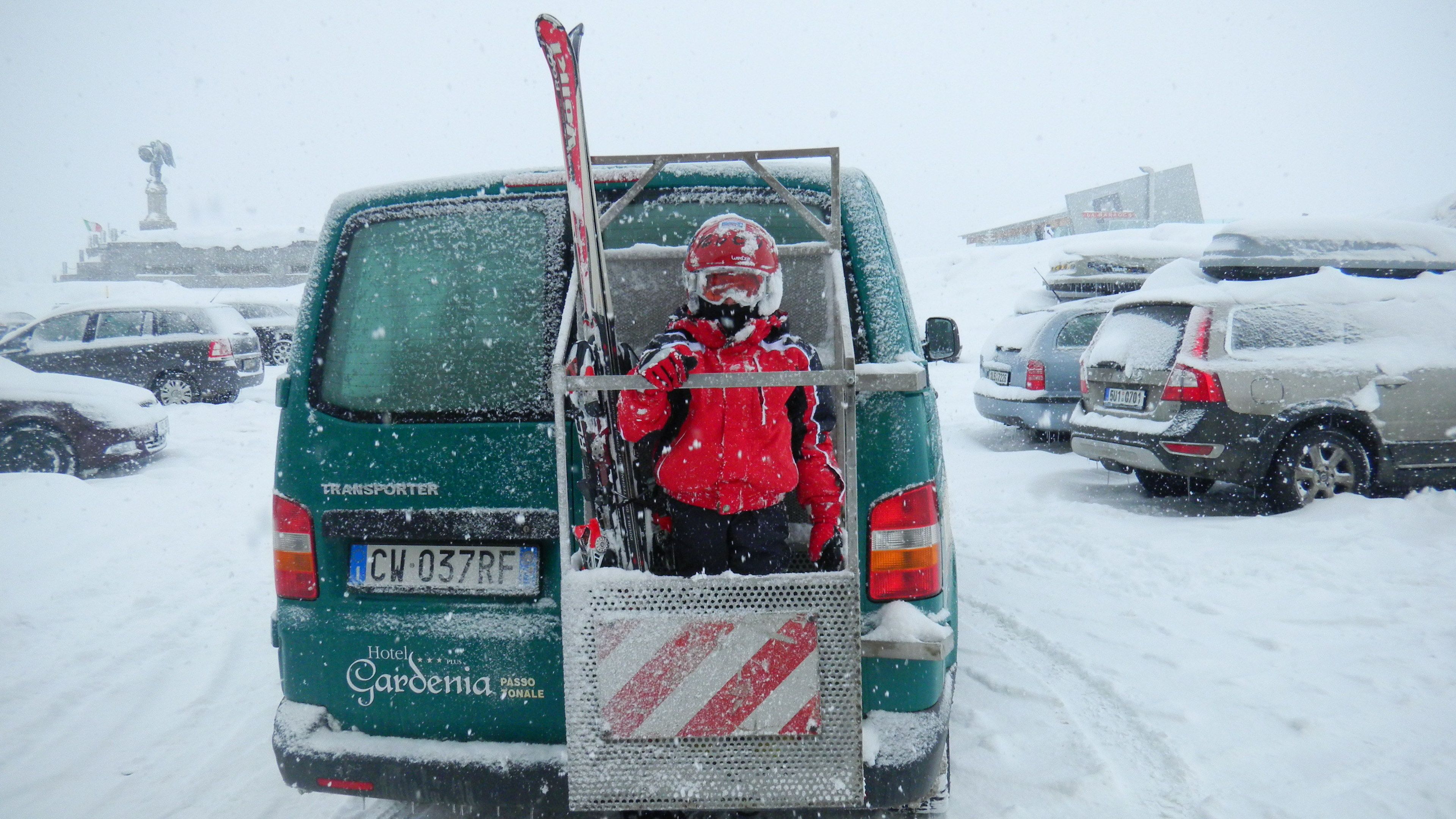 A green van with a ski rack and a person in a red jacket.