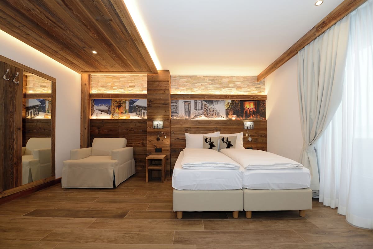 A modern hotel room with a wooden ceiling, a large bed with white linens, a seating area with a chair, and a wall-mounted TV.