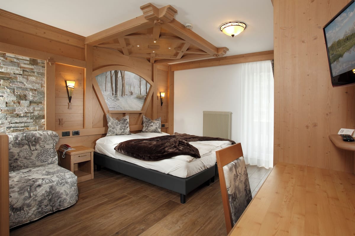 A cozy bedroom with a bed, a wooden headboard, a stone wall, a nightstand, a chair, and a television.