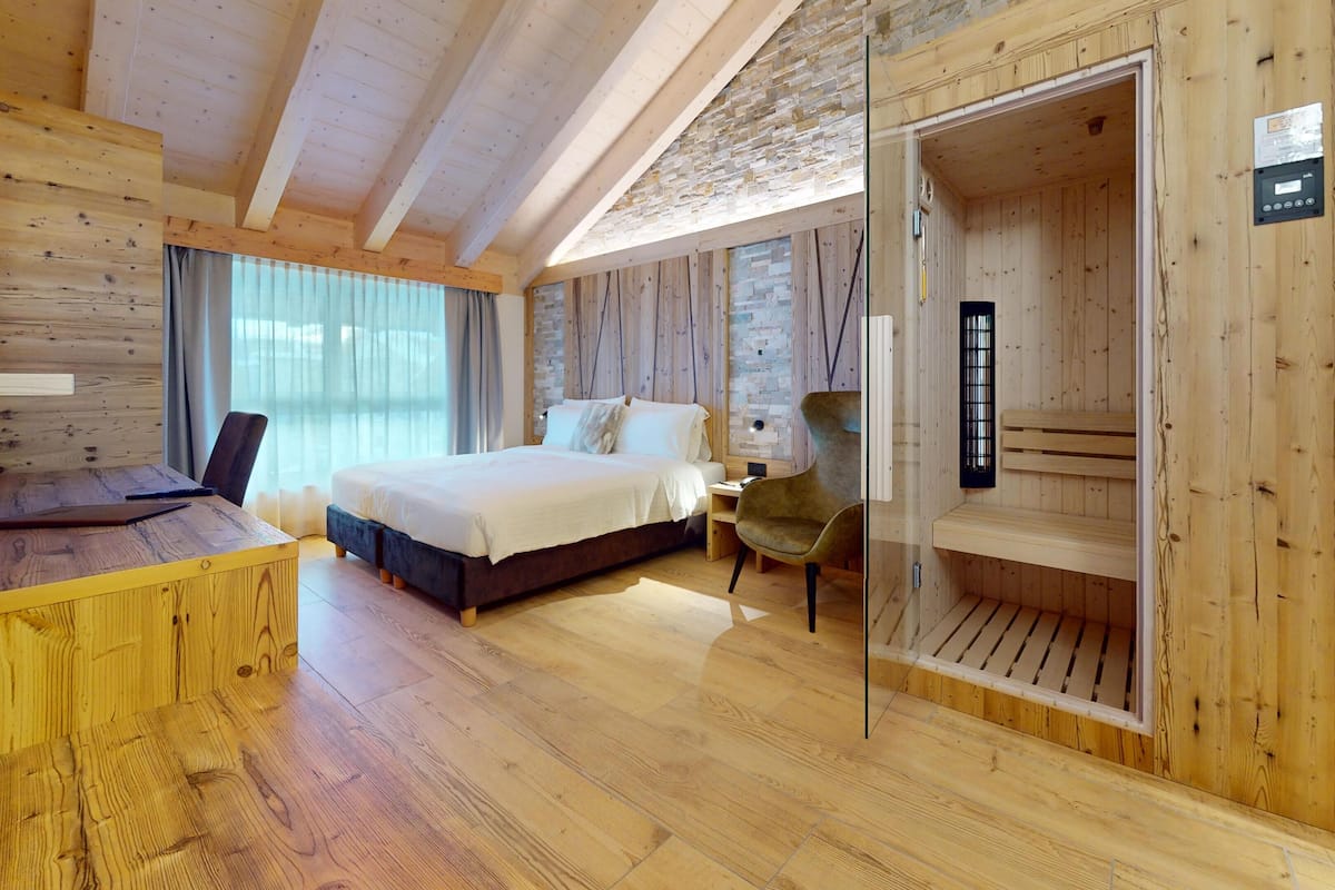 A wooden cabin room with a bed, desk, chair, and sauna.