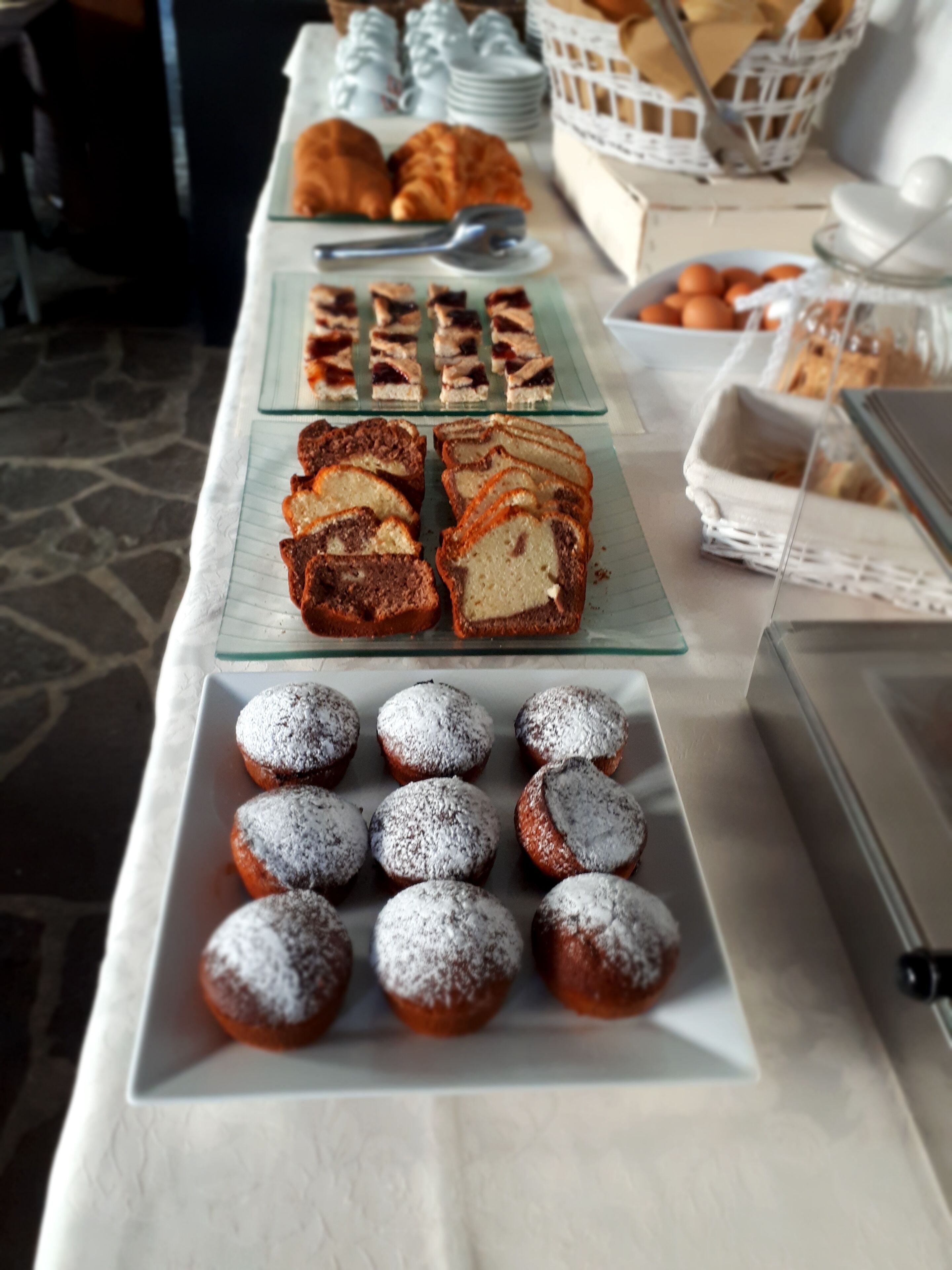 Una mesa de buffet con diversos pasteles y postres, incluyendo croissants, muffins y donuts cubiertos de azúcar glas.