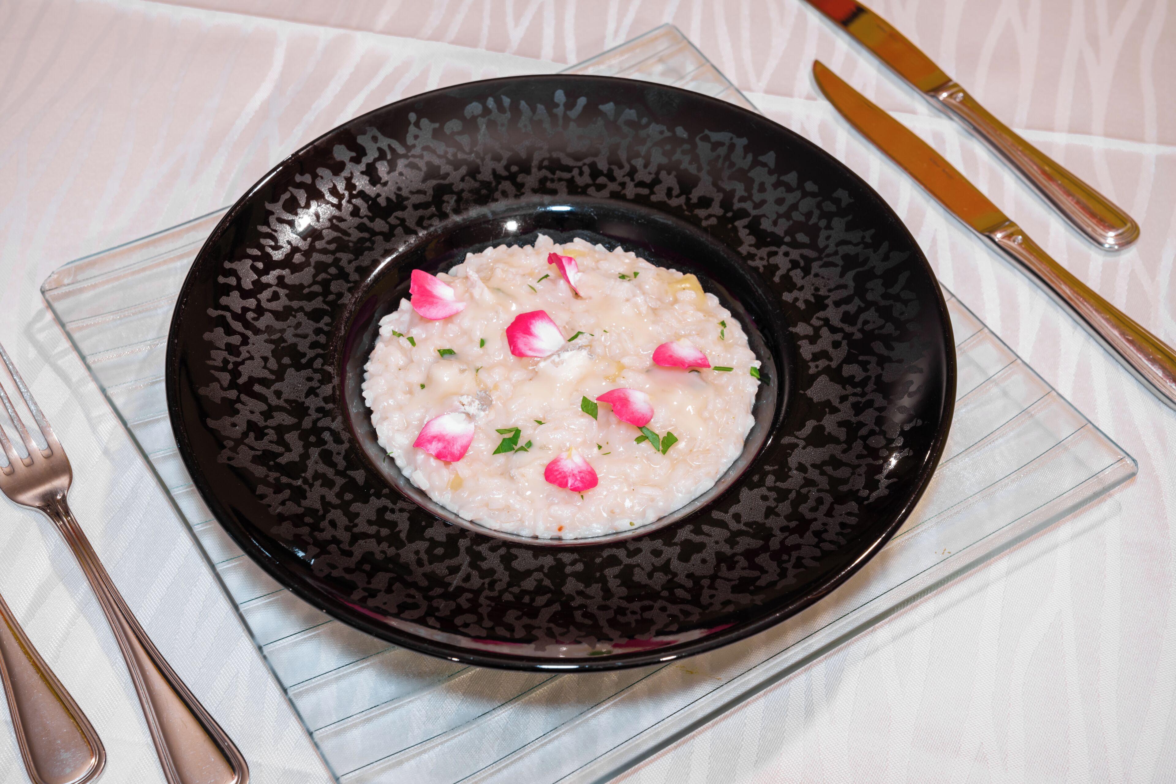 Um prato de risoto adornado com ervas e fatias de rabanete, servido em um prato preto com padrão.