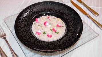Um prato de risoto adornado com ervas e fatias de rabanete, servido em um prato preto com padrão.
