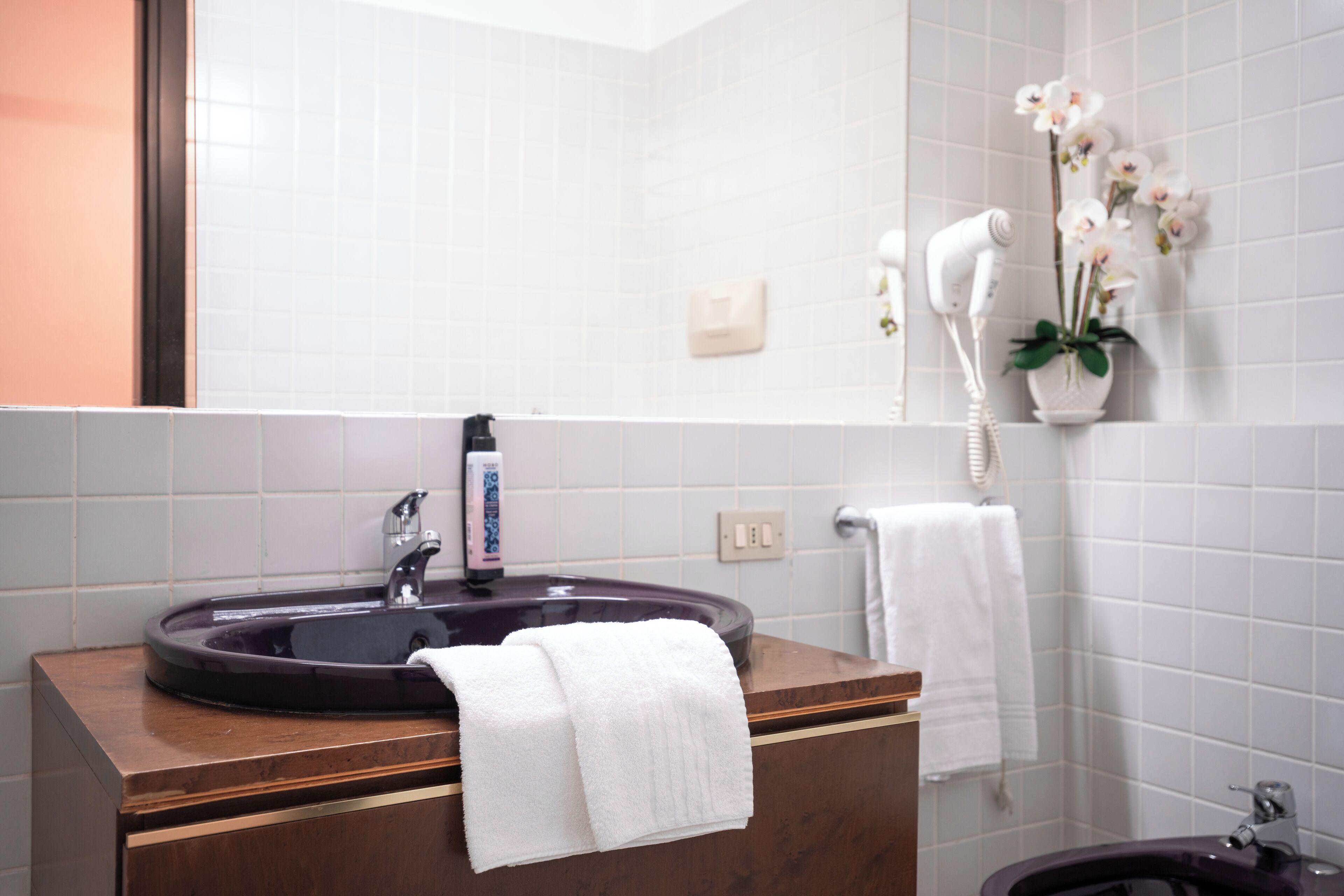 Un bagno con un lavandino rotondo, uno specchio, un asciugacapelli e un'orchidea in vaso.