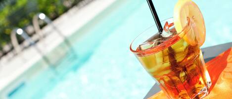 A glass of iced tea with a lemon slice and straw by a poolside.