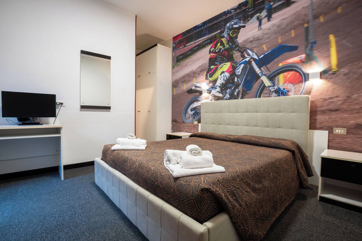 A hotel room with a large bed, a flat-screen TV, a desk, and a wall-mounted mirror.