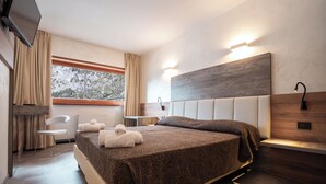 Habitación de hotel moderna con una cama grande, una silla, un escritorio y vistas a árboles desde la ventana.