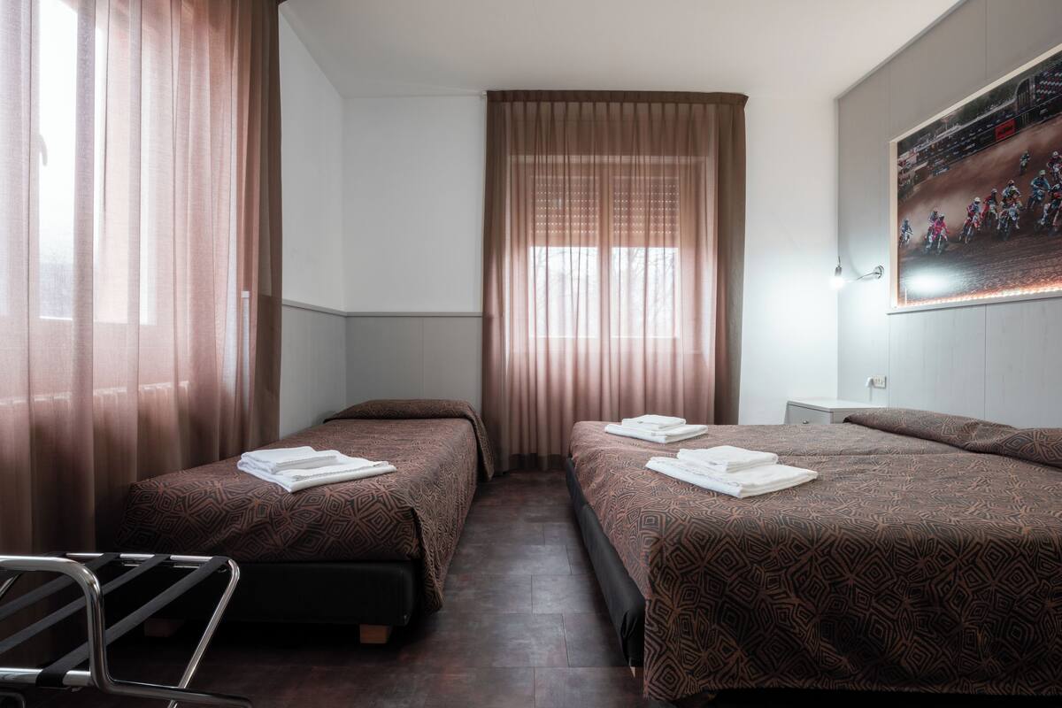 A hotel room with two beds, a desk, a chair, and a window with curtains.