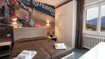 A hotel room with a bed, a nightstand, a window with a view of a mountain and construction site, and a wall with a motorcycle advertisement.