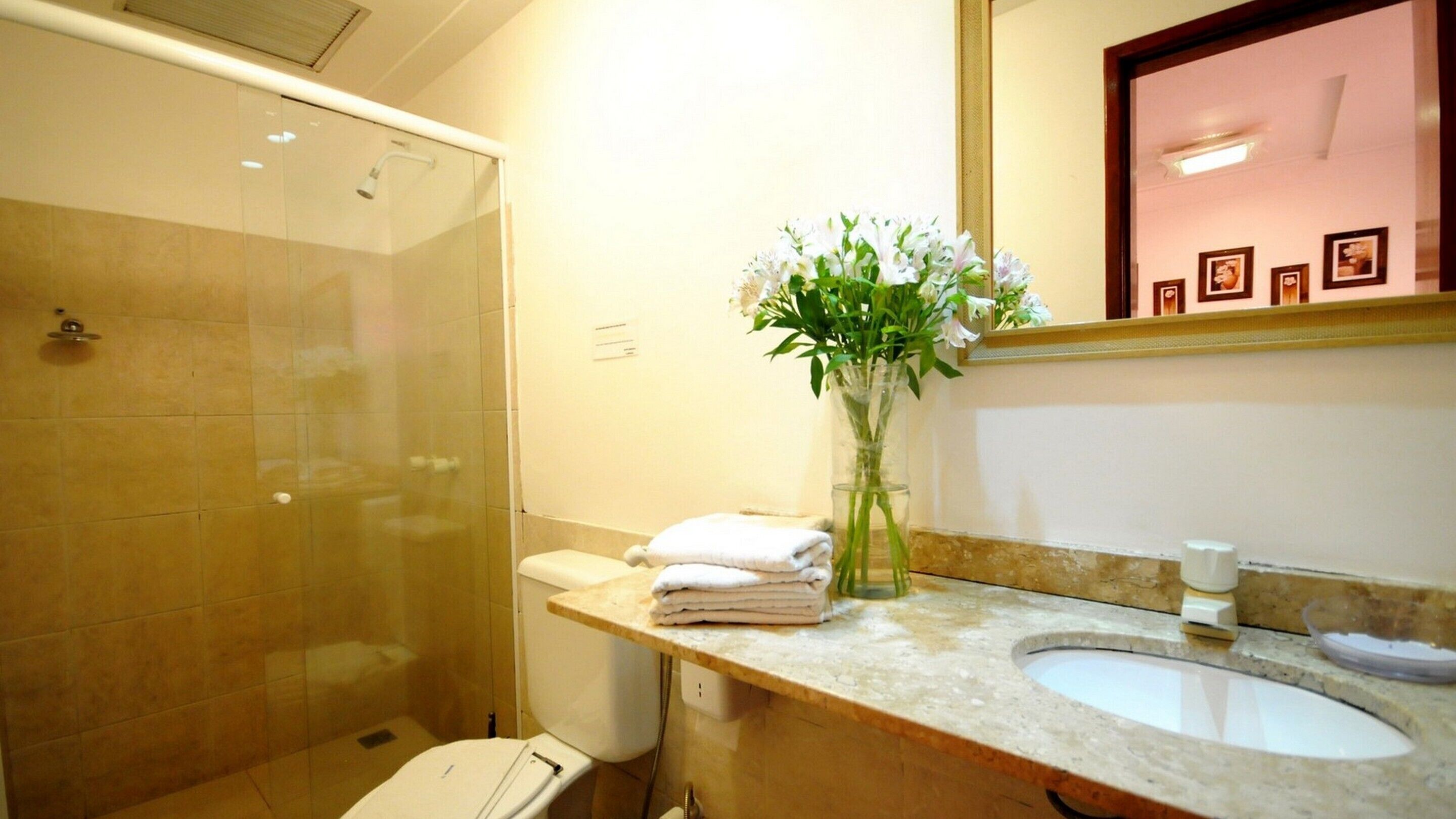 A bathroom with a glass-enclosed shower, a sink, a toilet, and a vase with flowers.