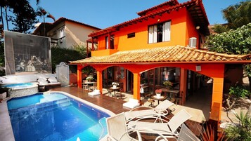 A two-story building with a swimming pool, outdoor seating, and a tiled roof.