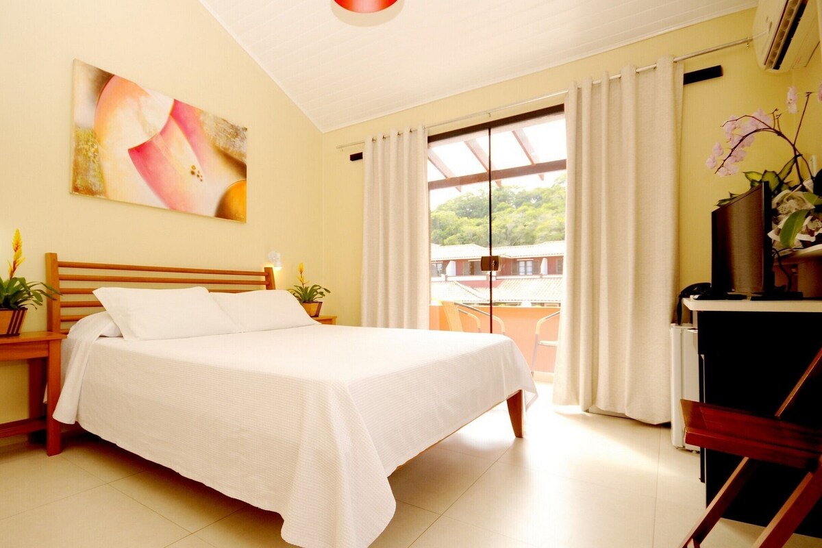A neatly arranged bedroom with a bed, bedside tables, a desk, and a window with curtains.