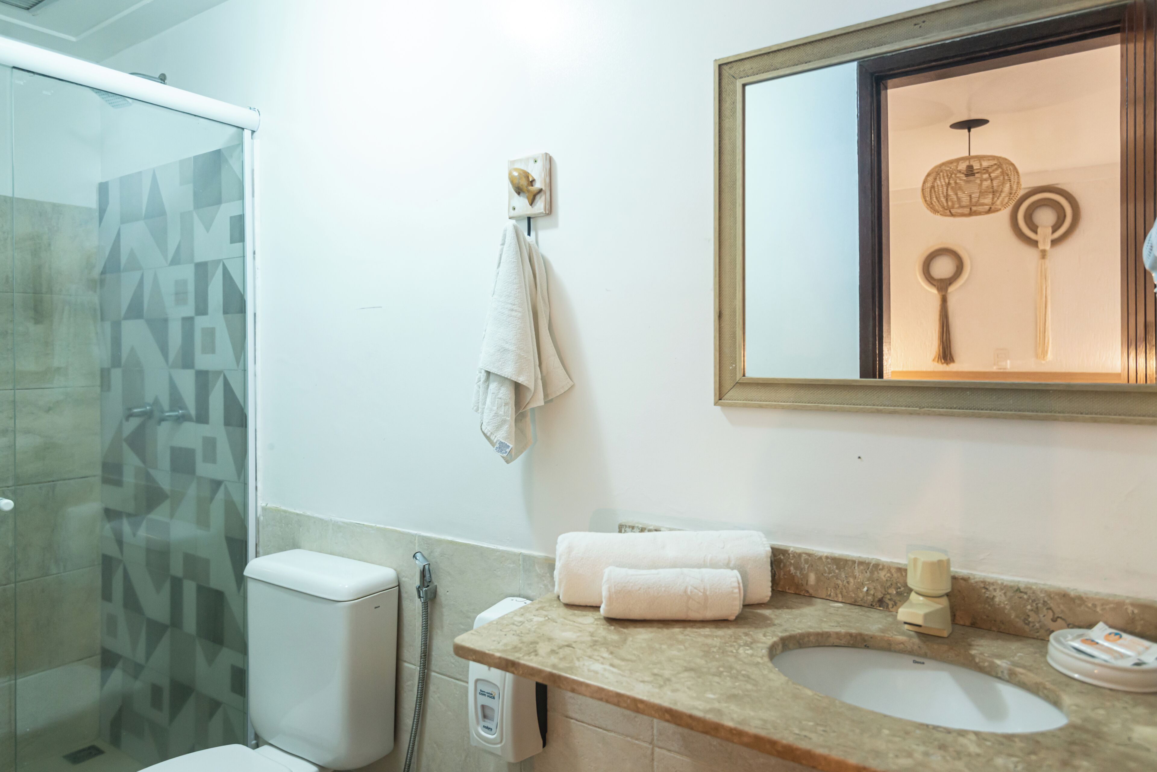 A bathroom with a glass shower enclosure, a toilet, a sink with a marble countertop, and a mirror with a wooden frame.
