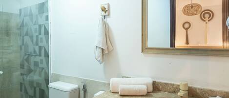 A bathroom with a glass shower enclosure, a toilet, a sink with a marble countertop, and a mirror with a wooden frame.