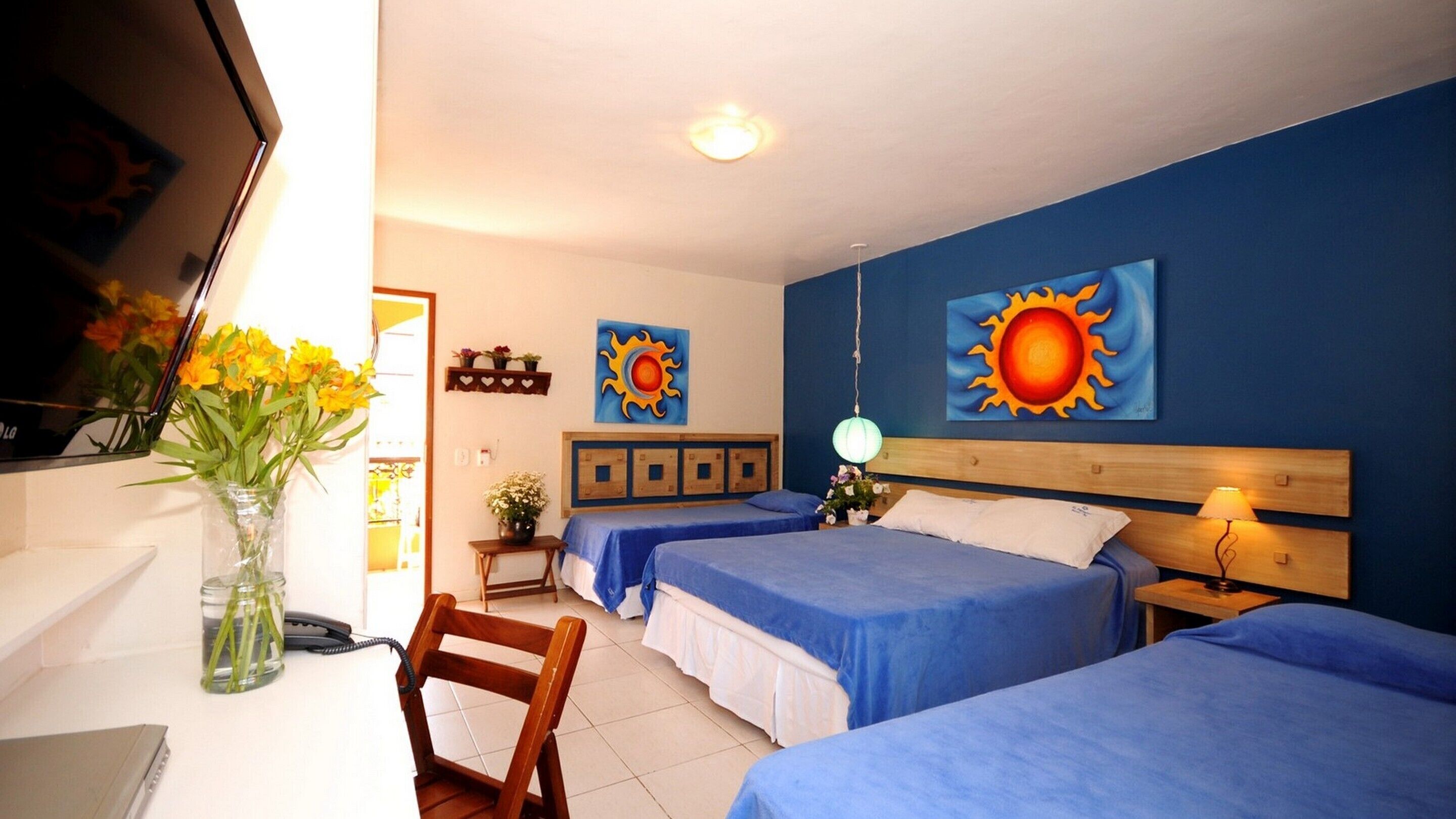 A hotel room with two beds, a desk with a chair, a vase with flowers, and wall art.