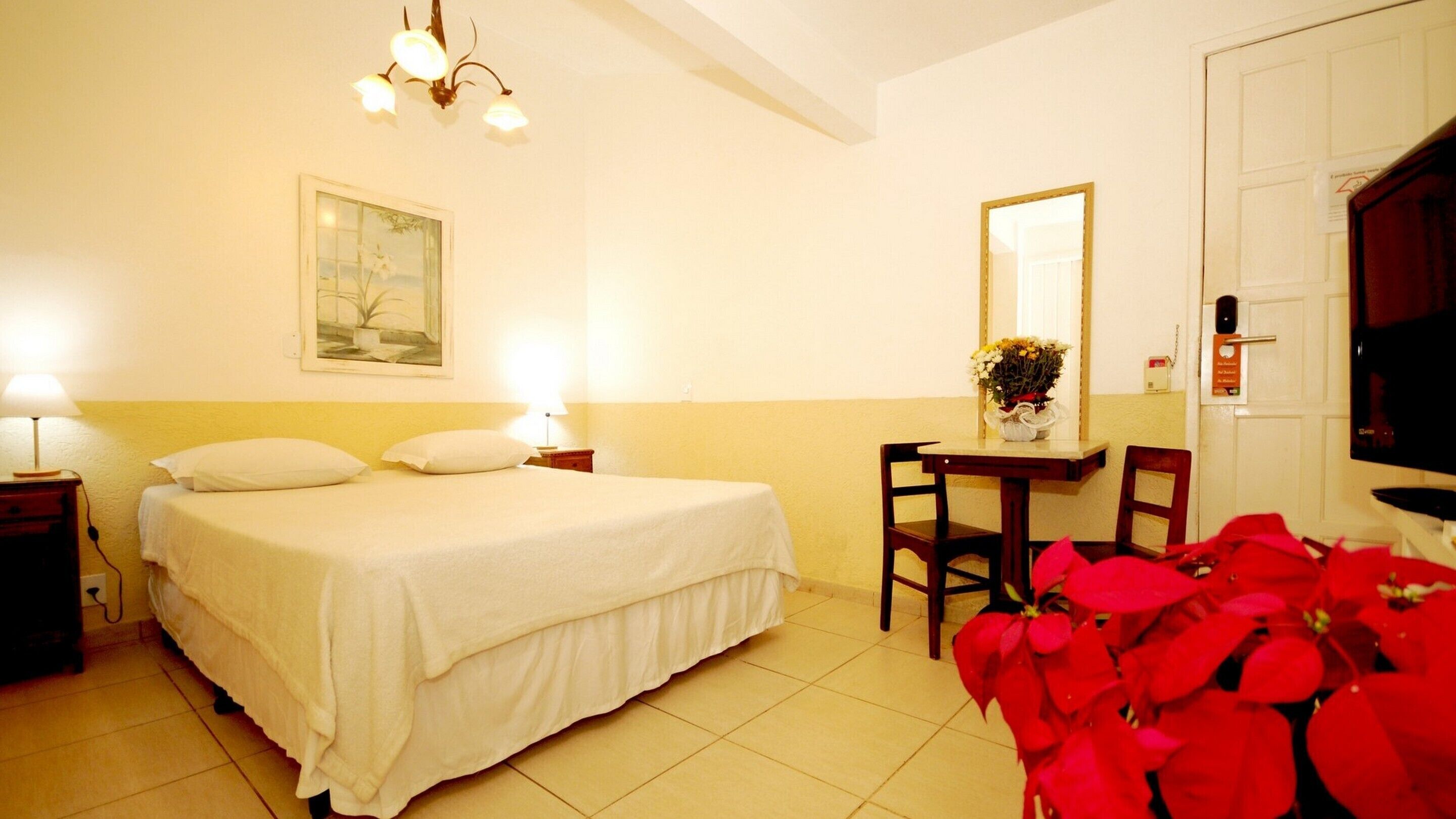 A hotel room with a bed, bedside lamps, a desk with a chair, a mirror, and a television.