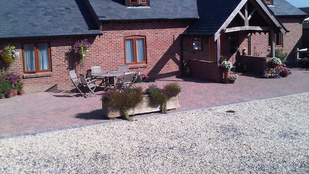 A brick house with a sloped roof, a porch with wooden railings, and a gravel driveway. - The Old Dairy Farm (Emsworth)