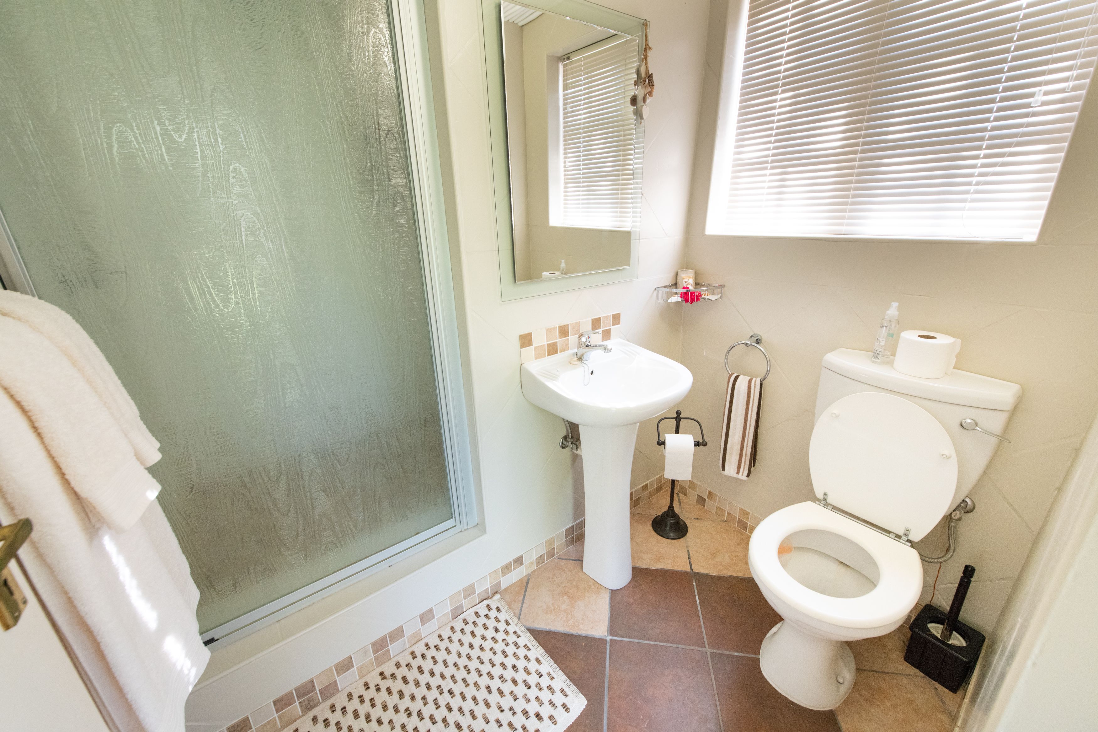 Un baño con mampara de vidrio, lavabo, inodoro y espejo.