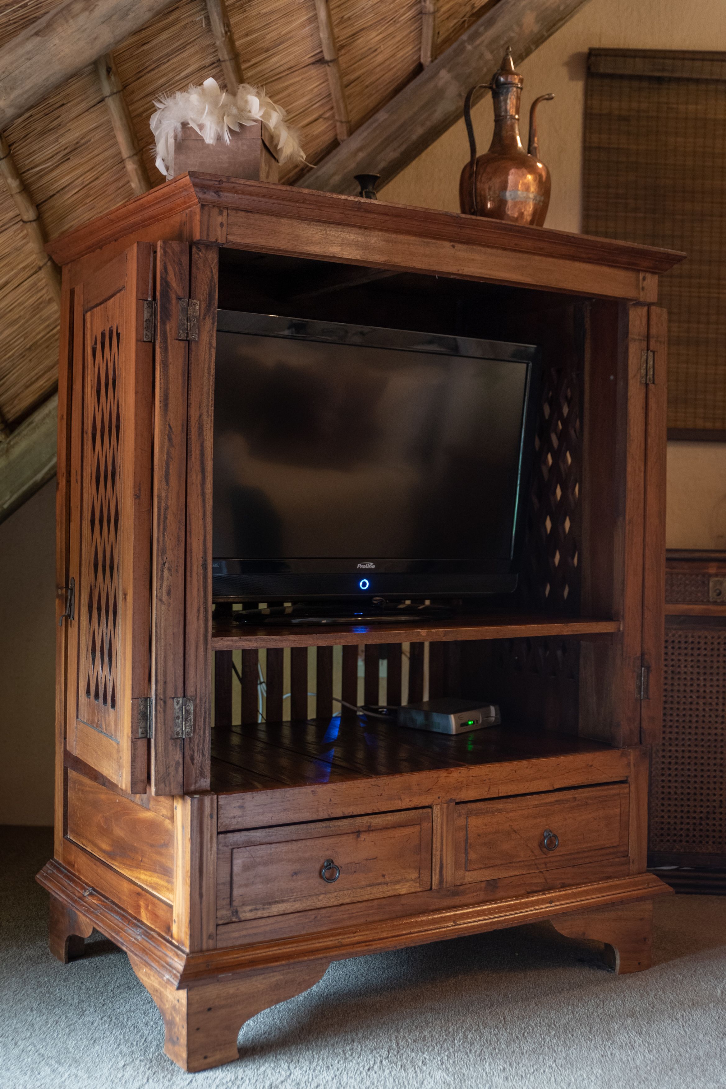 A wooden entertainment center with a flat-screen TV, a decorative vase, and a small shelf.