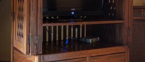 A wooden entertainment center with a flat-screen TV, a decorative vase, and a small shelf.