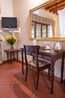 Una mesa de comedor de madera con una silla, un jarrón de flores, un televisor sobre un mueble bajo y un espejo grande en la pared.