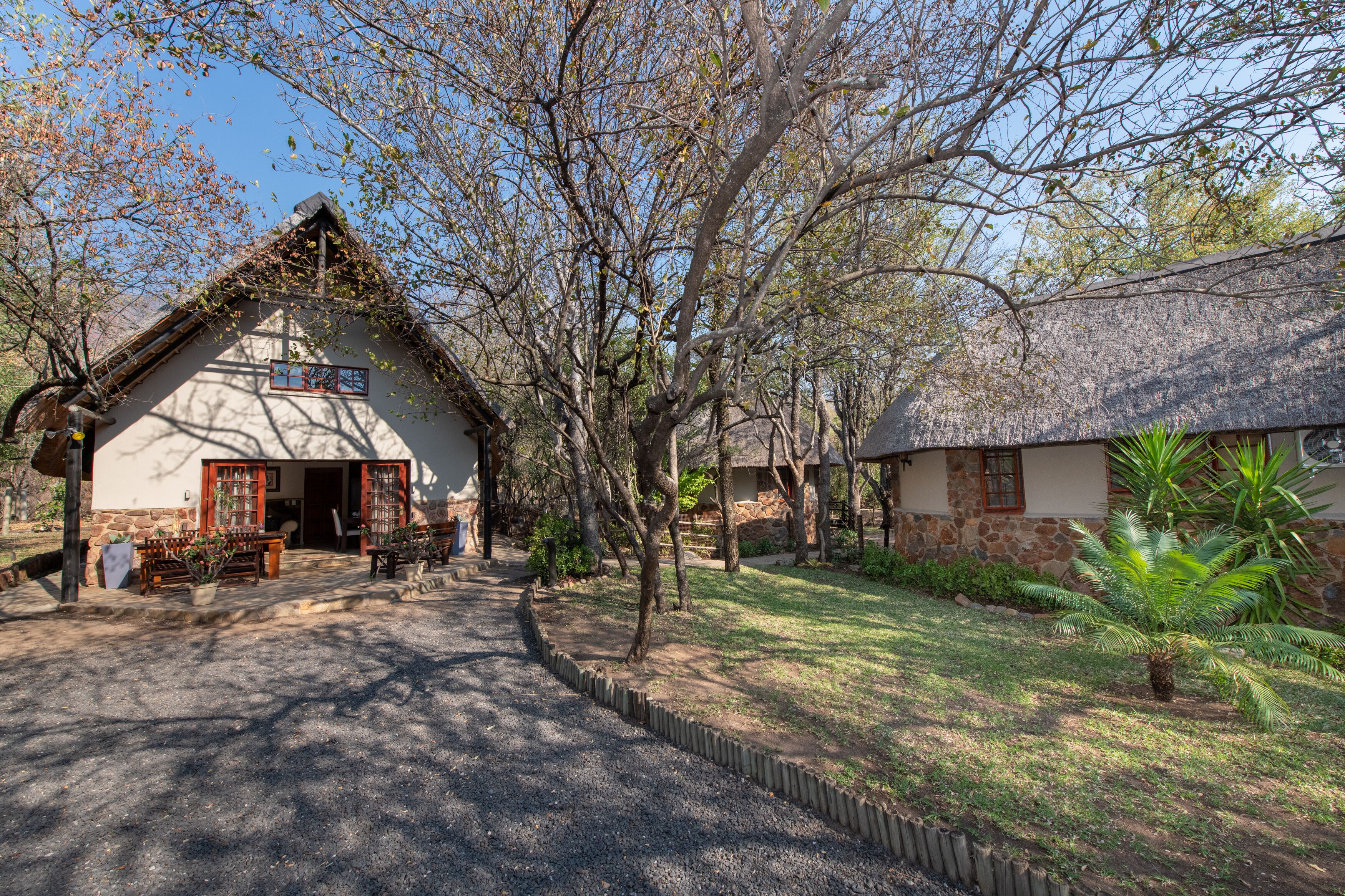 A rustic building with a thatched roof, surrounded by trees and a well-maintained lawn.