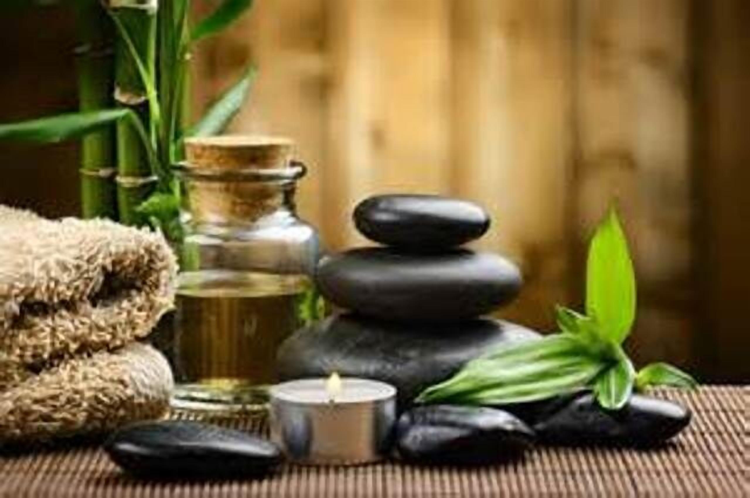 A spa setting with a bamboo plant, a candle, a stack of black stones, and a towel.
