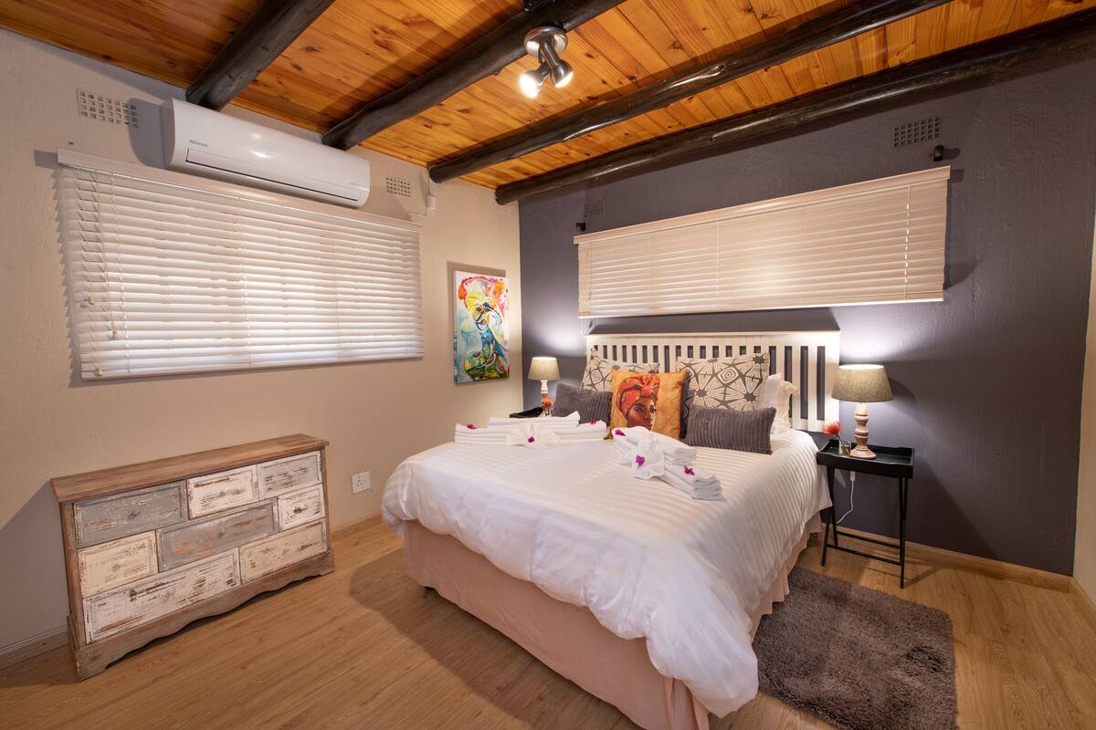 A bedroom with a wooden ceiling, a bed with white bedding, a dresser, and two bedside lamps.