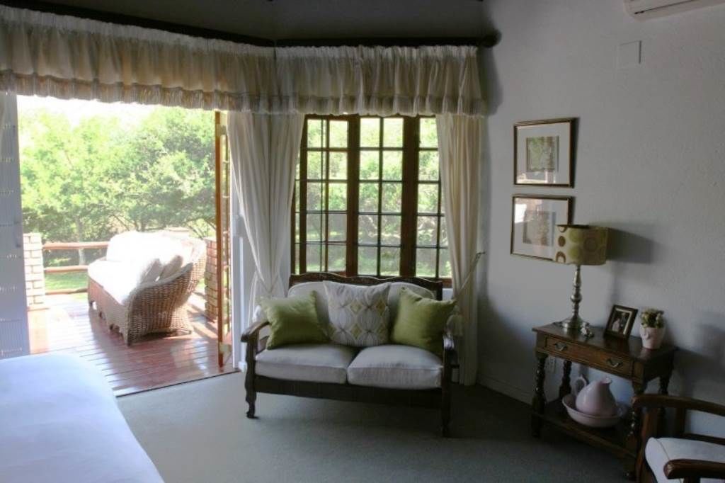 A cozy room with a sofa, a small table with a lamp, and a window with curtains.