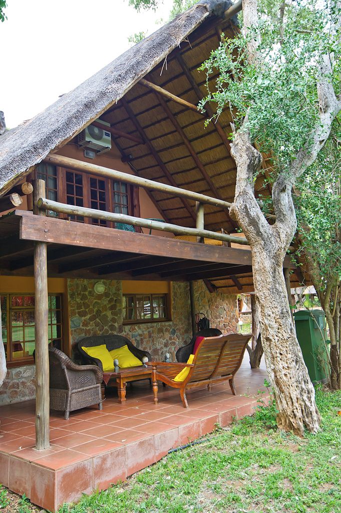 A rustic building with a thatched roof, a stone wall, and a wooden porch with wicker furniture.