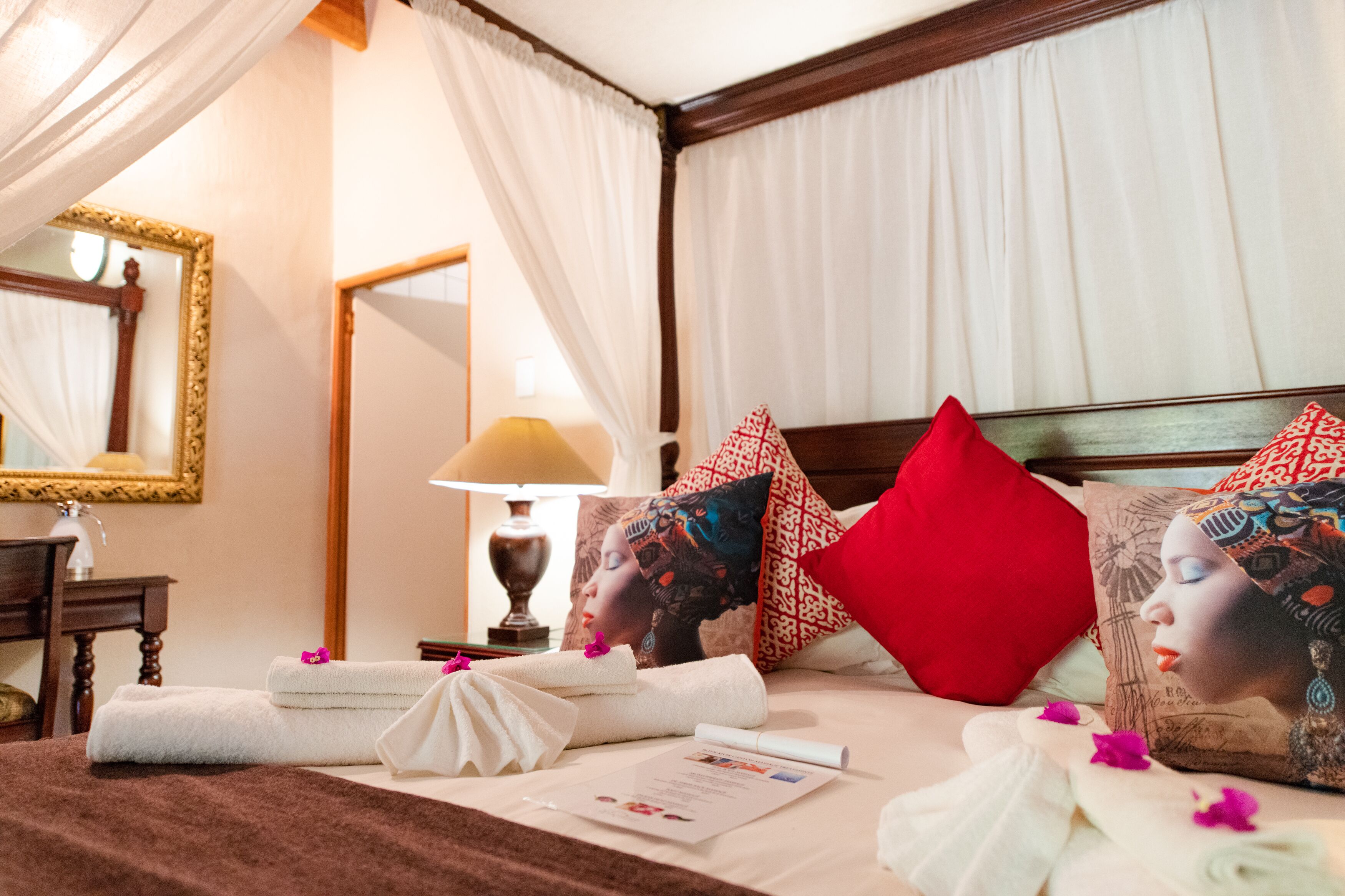 A neatly made bed with a red pillow, white towels, and a floral arrangement.