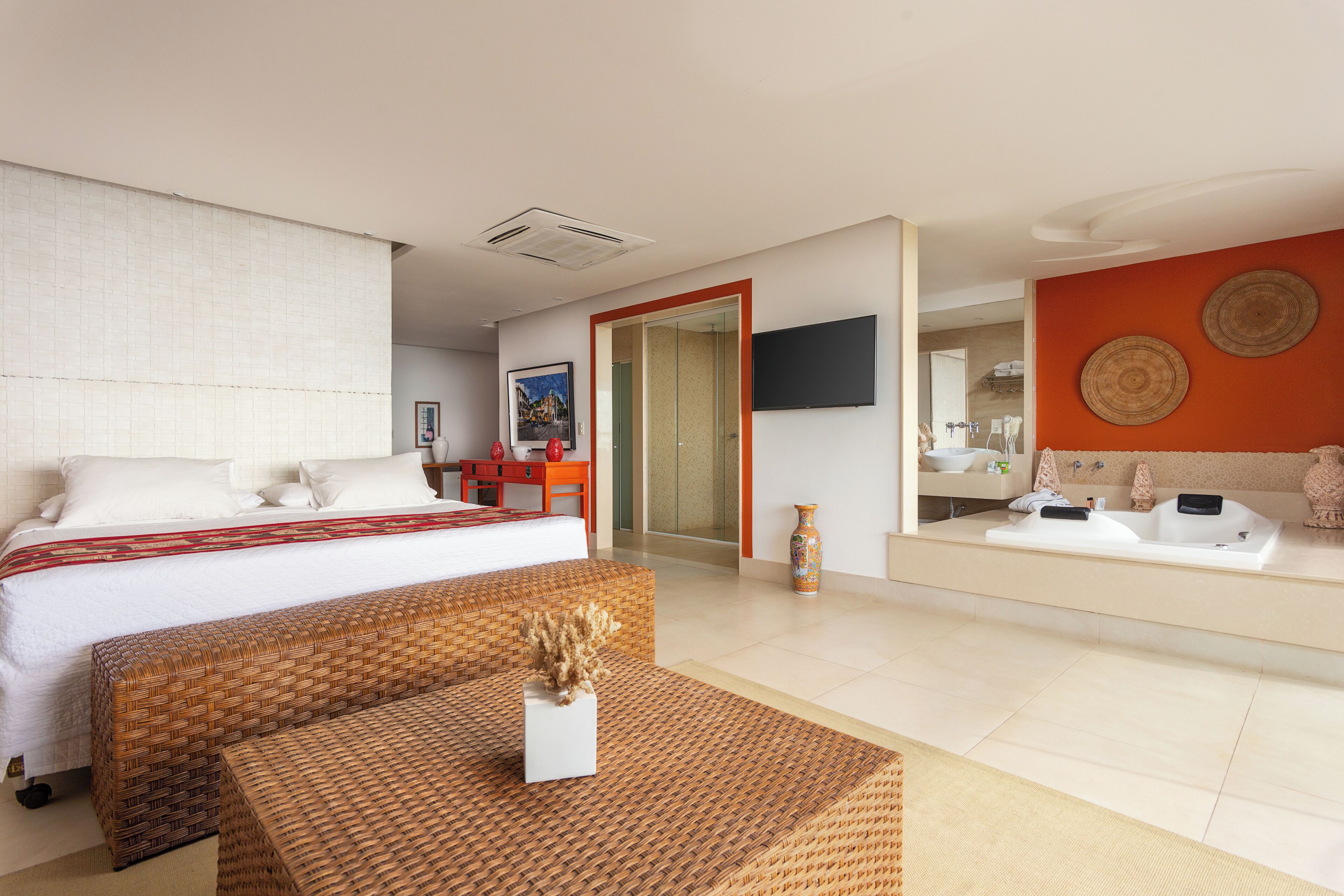 A hotel room with a bed, a sitting area with a table, a bathroom with a mirror and sink, and a television mounted on the wall.