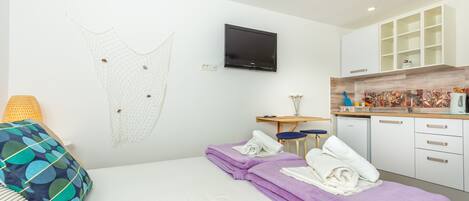 A modern hotel room with a bed, a desk, a television, and a kitchenette.