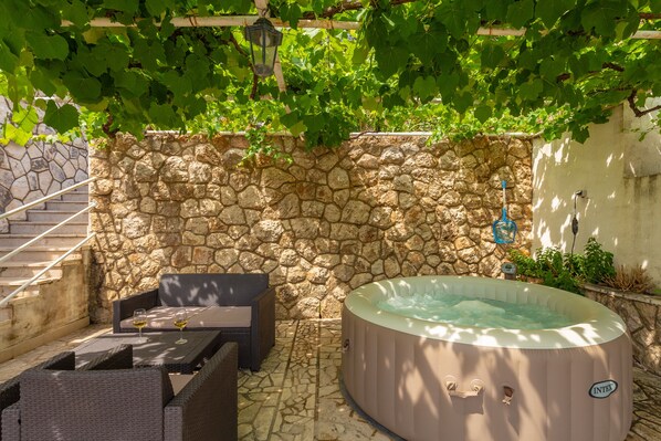 A stone wall, a wicker sofa, and a hot tub in an outdoor setting.