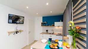 Una cocina moderna con una pared azul de acento, una zona de comedor con una mesa para dos, y un televisor montado en la pared.
