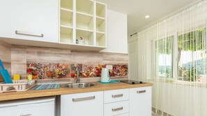 Una cocina moderna con armarios blancos, encimera de madera y salpicadero con motivos de frutas y verduras.