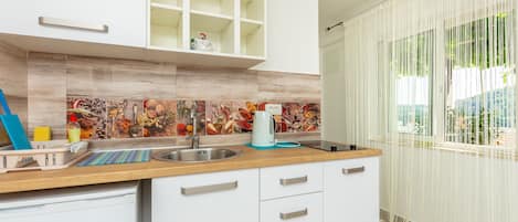 Una cocina moderna con armarios blancos, encimera de madera y salpicadero con motivos de frutas y verduras.