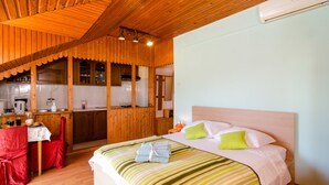 Una habitación acogedora con techo de madera, una cama con ropa de cama verde y blanca, una pequeña cocina con fregadero y armarios, y una silla roja.