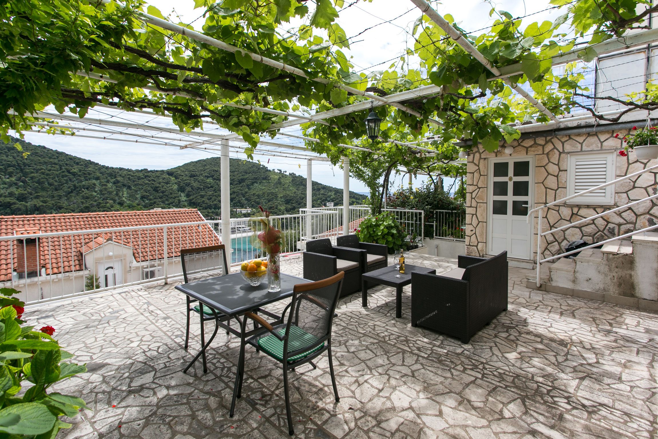 Une terrasse extérieure avec un sol en pierre, une table et des chaises, et une vue sur une montagne.
