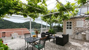 Um pátio ao ar livre com chão de pedra, uma mesa com cadeiras e vista para uma montanha.