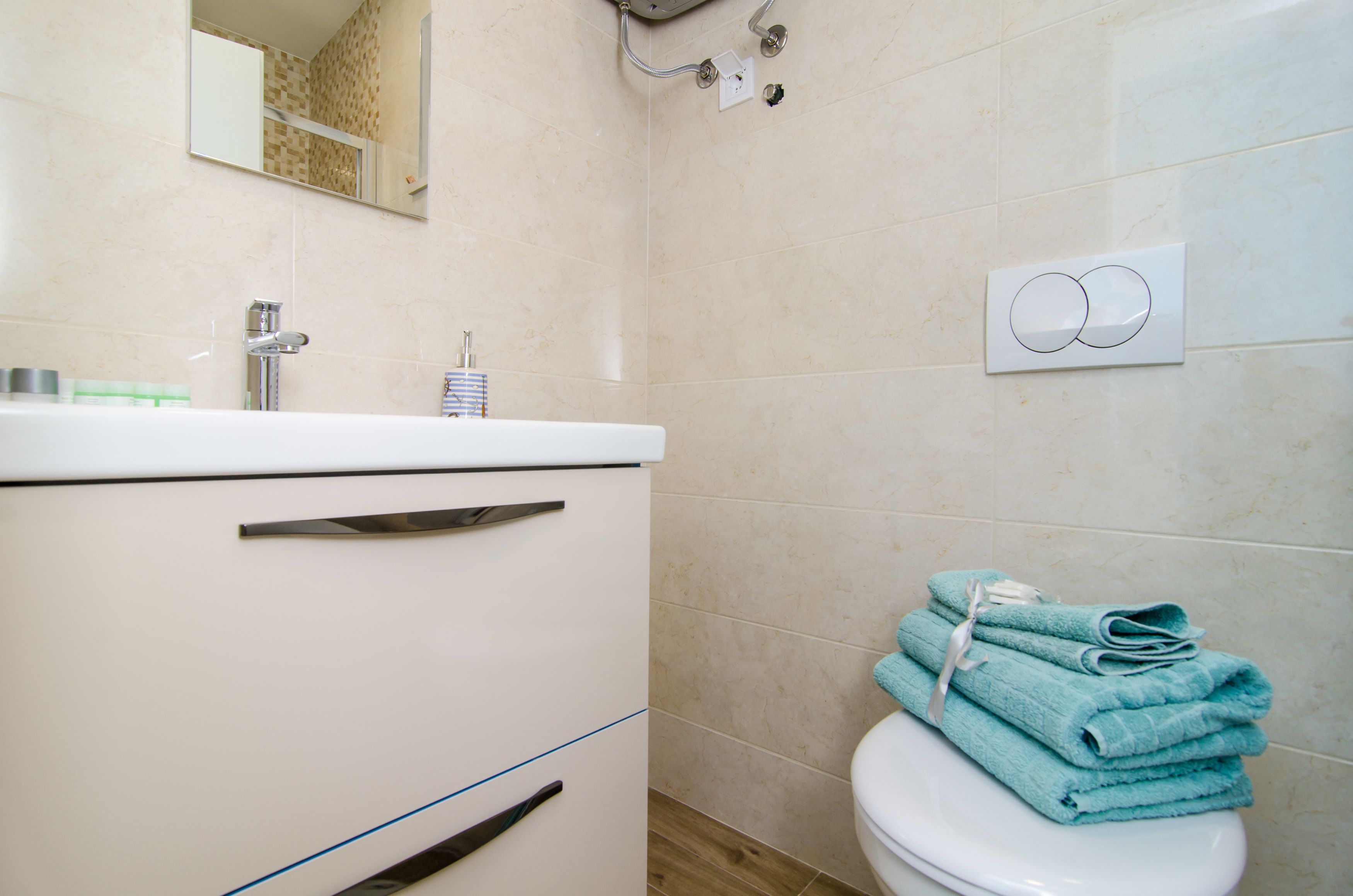 A bathroom with a white sink, mirror, and toilet. There are towels stacked on the toilet.