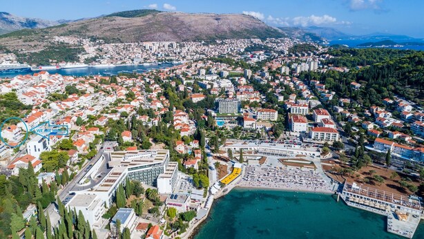 Vista aérea de uma cidade costeira com um porto de iates, edifícios residenciais e uma área de praia.