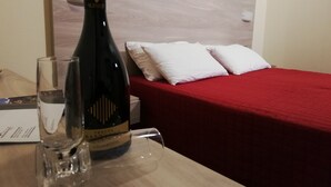 A bottle of Tenuta San Marco Prosecco on a wooden table with a glass, in a room with a red bedspread and white pillows. - Des Alpes (Castione della Presolana)