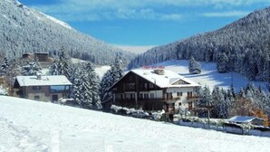 A snow-covered mountain lodge with a wooden exterior, surrounded by snow-laden trees and a clear sky. - Des Alpes (Castione della Presolana)