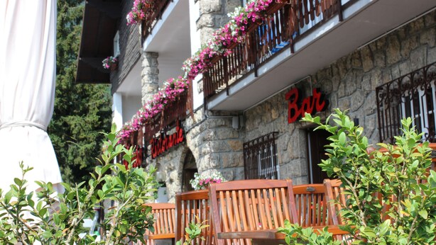 A stone building with a bar sign, wooden balcony railings, and potted plants. - Des Alpes (Castione della Presolana)