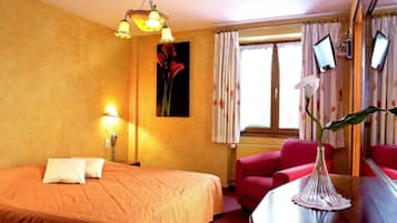 Een hotelkamer met een bed, een bureau met een vaas, een stoel, een lamp, een schilderij en twee schermen aan de muur.