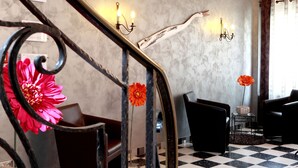 A hotel lobby with a checkered floor, black leather chairs, a staircase with a metal railing, and wall-mounted sconces. - A la Vignette (Saint-Hippolyte)