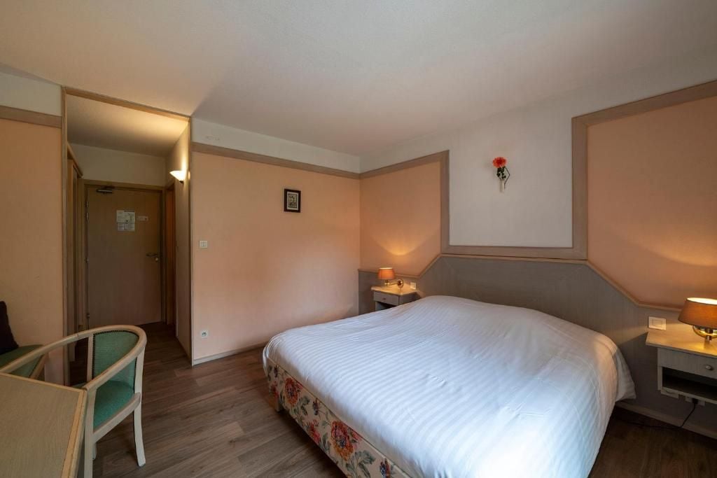 A hotel room with a bed, a chair, a bedside table with a lamp, and a wall-mounted picture.