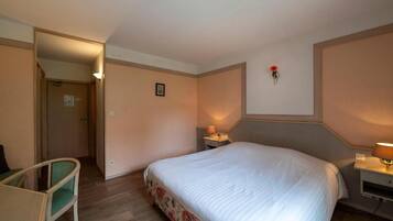 A hotel room with a bed, a chair, a bedside table with a lamp, and a wall-mounted picture.